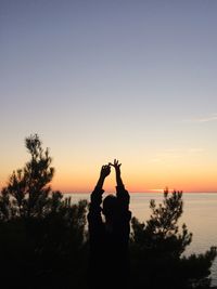 Silhouette man hand by tree against sky during sunset