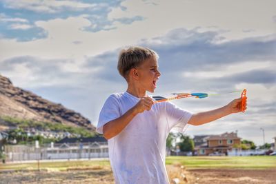 Boy playing with airplane on field against sky