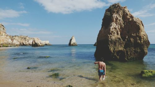 Rear view of boy standing in sea against rock