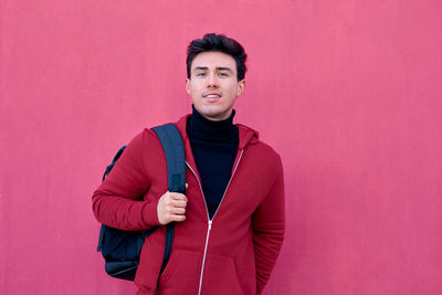 Portrait of young man standing against pink background