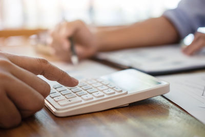 Cropped image of colleagues with calculator analyzing data on desk