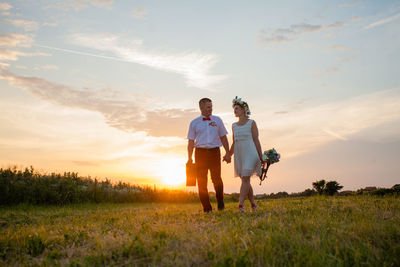 Friends on field against sky during sunset