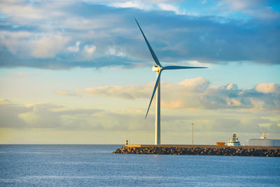 View of sea bay and large windmill at edge of stone breakwater