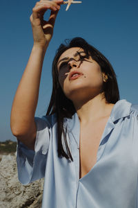 Portrait of beautiful young woman standing against blue sky