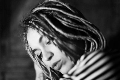 Close-up of young woman with dreadlocks looking away in dark