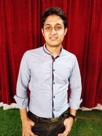 Portrait of smiling young man standing against red curtain