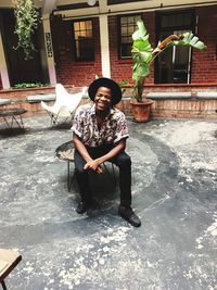 Full length portrait of young man sitting against building