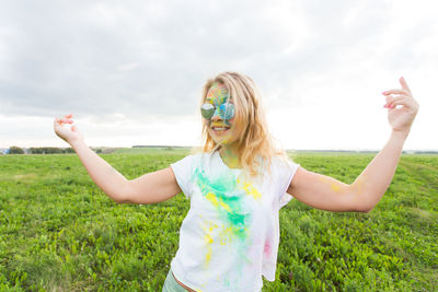 Happy woman with arms raised on field against sky