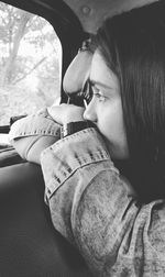 Close-up of thoughtful young woman looking through window in car