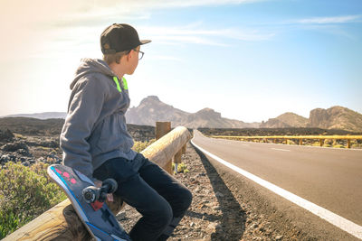 Boy sitting by road on railing