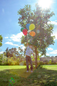 Full length of person holding balloons on field against trees