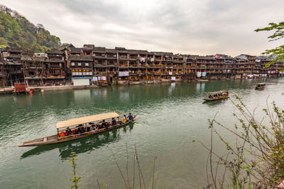 Boats in river by buildings against sky