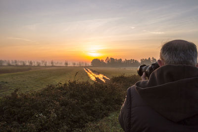 Rear view of man photographing at sunset