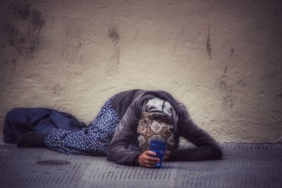 Beggar kneeling on sidewalk against wall