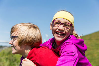 Cheerful siblings piggybacking on sunny day