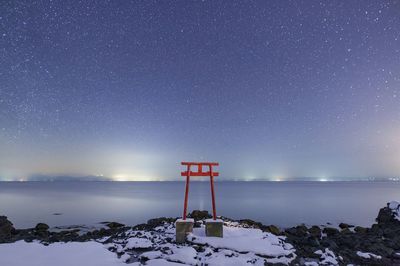 Torii gate on field against sea during winter at night