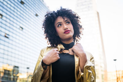 Fashionable young woman with curly hair standing in city