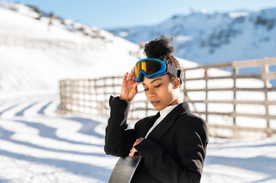 African american woman with goggles and a snowboard on a snowy mountain during winter