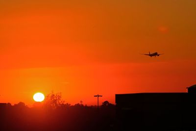 Low angle view of silhouette airplane against orange sky