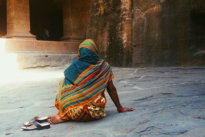 Rear view of woman sitting on walkway by temple