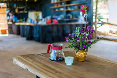 Coffee by vase on wooden table at cafe