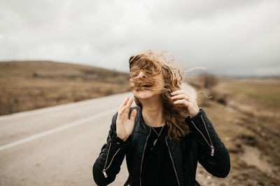 Portrait of young woman standing on road against sky