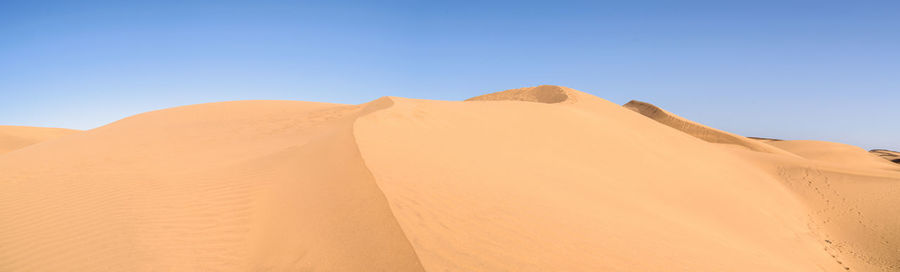 Sand dunes in desert against clear blue sky