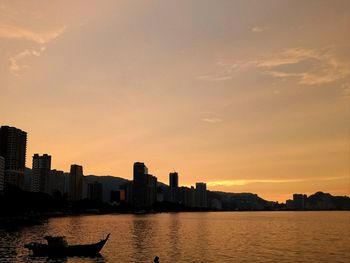 River by silhouette city against sky during sunset