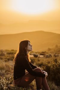 Side view of young woman looking away at sunset