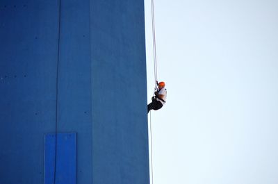 Low angle view of man working on building against clear blue sky