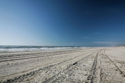 Tire tracks on beach against clear blue sky