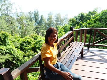 Portrait of smiling boy sitting on wood against trees