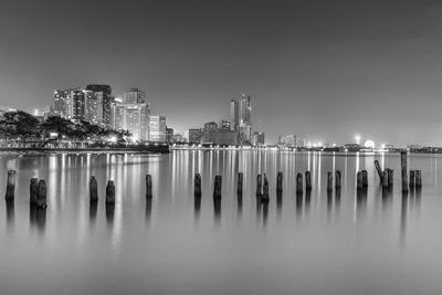 Wooden posts in sea by city against sky