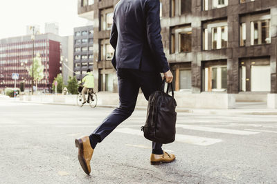 Low section of male entrepreneur with bag crossing street
