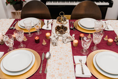 From above of table setting with glasses and cutlery near plates decorated with candles and cones for christmas celebration