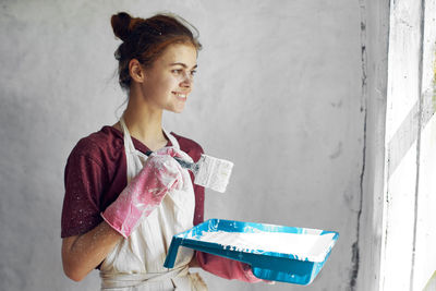 Young woman reading book while standing against wall