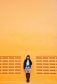 Portrait of woman standing against orange wall