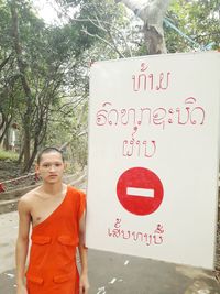 Portrait of man standing by sign board against trees