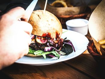 Cropped hand of person holding knife over burger