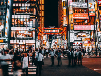 People on city street amidst illuminated buildings at night