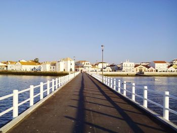 Footbridge over river in city against clear blue sky