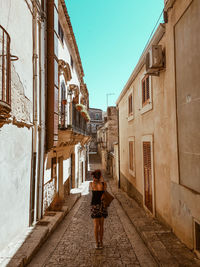 Rear view of man standing on narrow alley amidst buildings in city