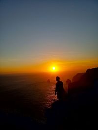 Silhouette people on sea against sky during sunset