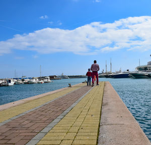 Rear view of man on pier at harbor against sky