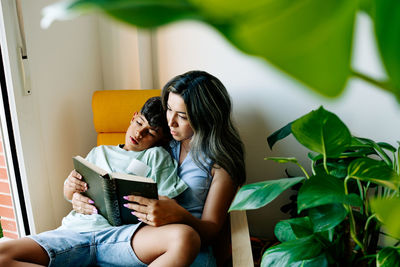 Young family mother and son reading a book in sofa at home