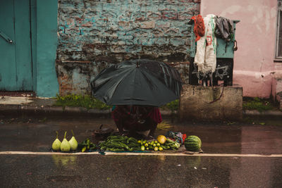 Rear view of woman with umbrella standing by wet wall