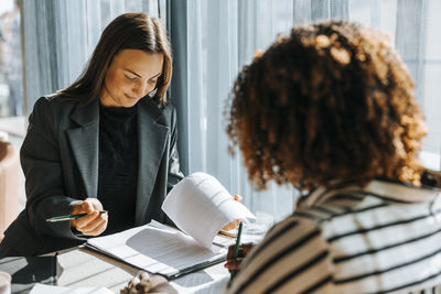 Female business professional reviewing contract while sitting with client at office