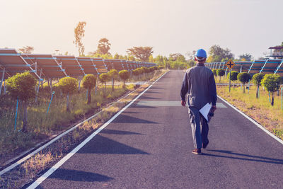 Rear view of man walking on road against sky