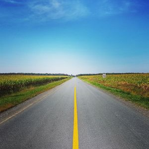 Road amidst field against clear blue sky