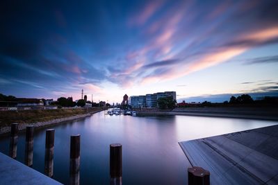 Scenic view of river by buildings against sky at sunset